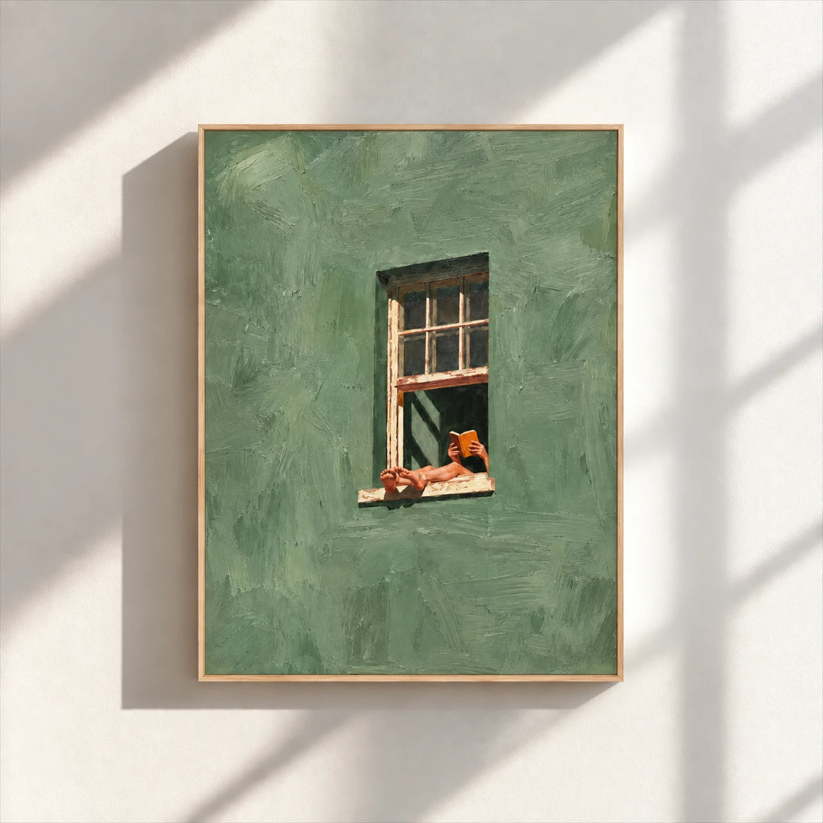 Sage green window artwork with a reader, displayed in a light wood-tone frame on a sunlit wall.
