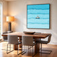 Blue car and surfer artwork above a wood dining table with upholstered chairs and a warm table lamp.