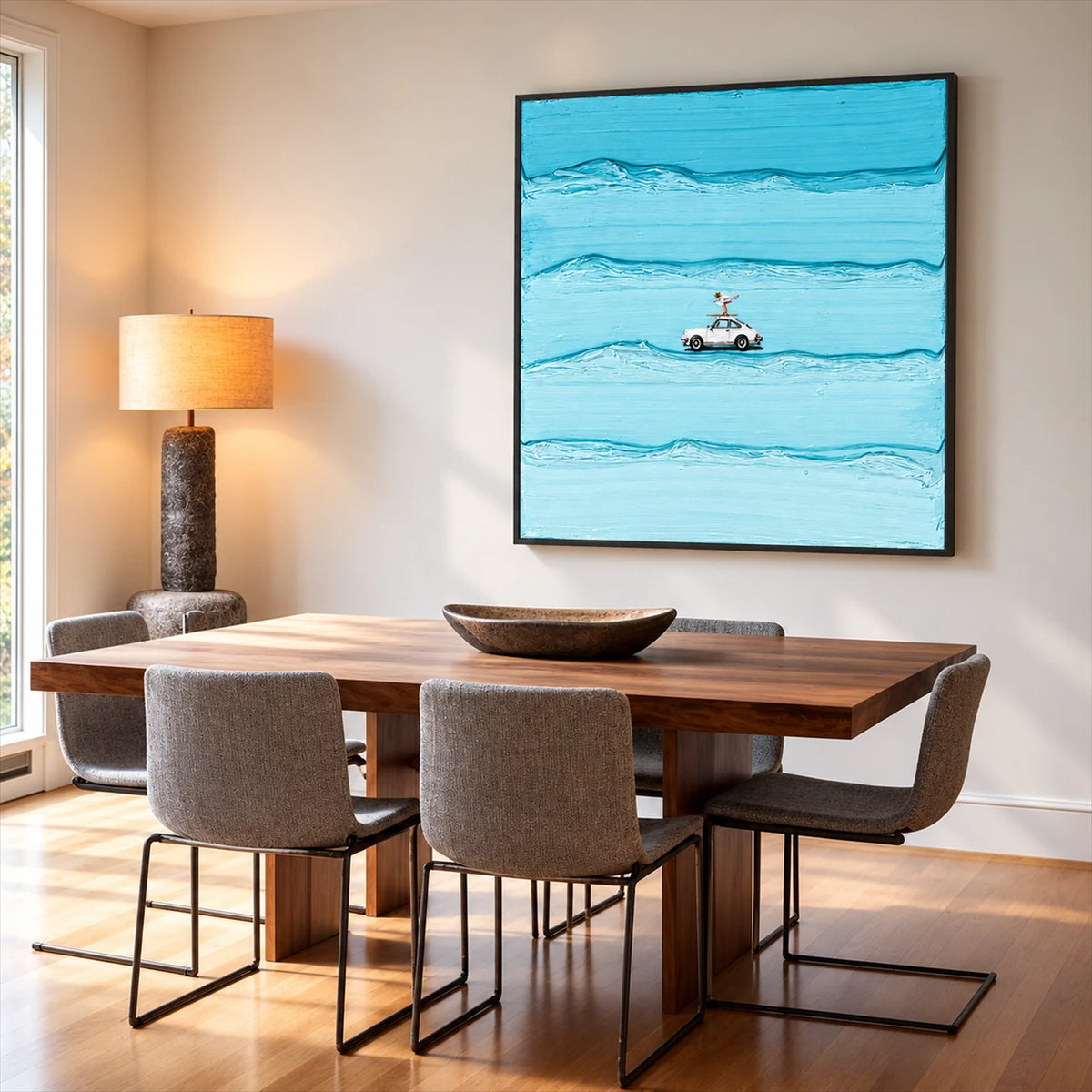 Blue car and surfer artwork above a wood dining table with upholstered chairs and a warm table lamp.
