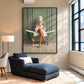 Bath reader painting in a black frame above a blue chaise longue beside tall windows.