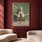 Bath reader painting in a gold frame on a deep red wall above cream-colored lounge chairs.