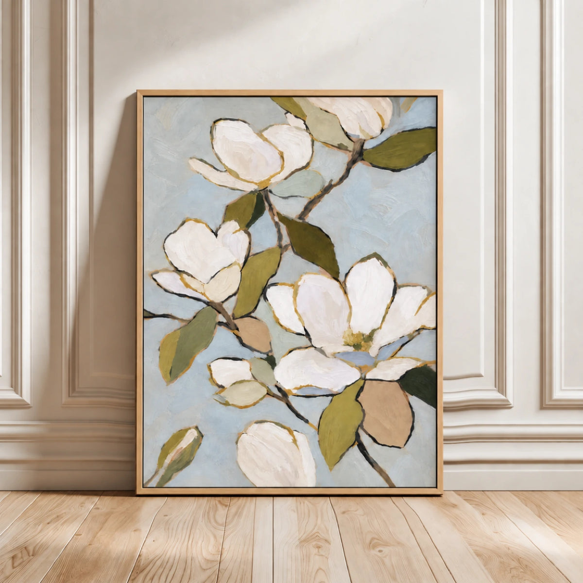 Gold-framed magnolia painting leaning against decorative wall panels on a wood floor.