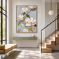 Magnolia wall art above a sage console beside a sunlit staircase.