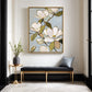 Gold-framed magnolia wall art above a black bench with a blue cushion beside a tall window.