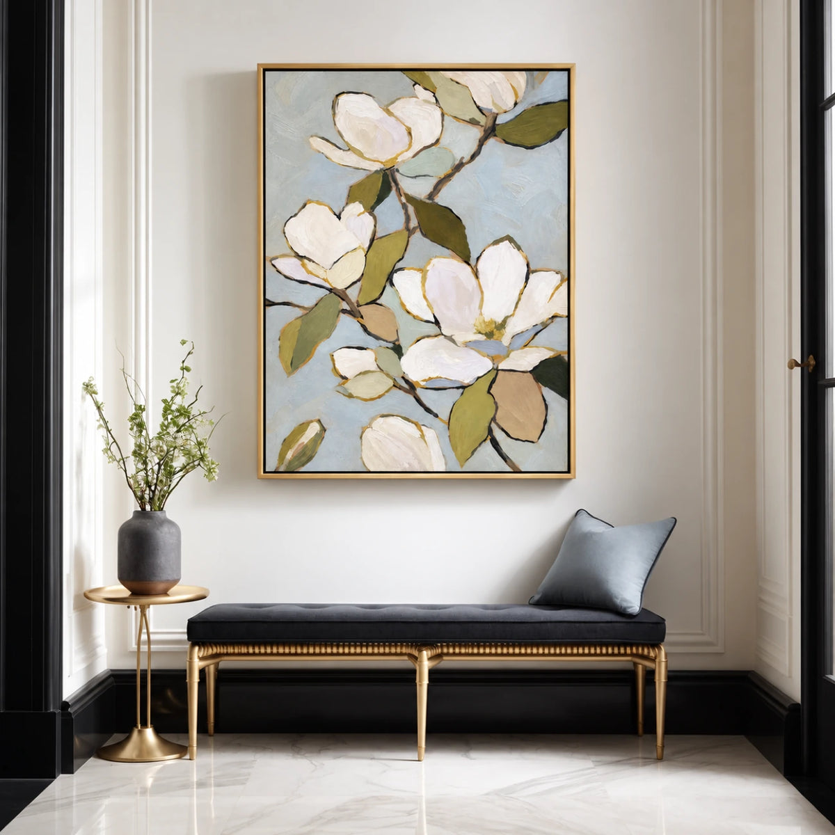Gold-framed magnolia wall art above a black bench with a blue cushion beside a tall window.