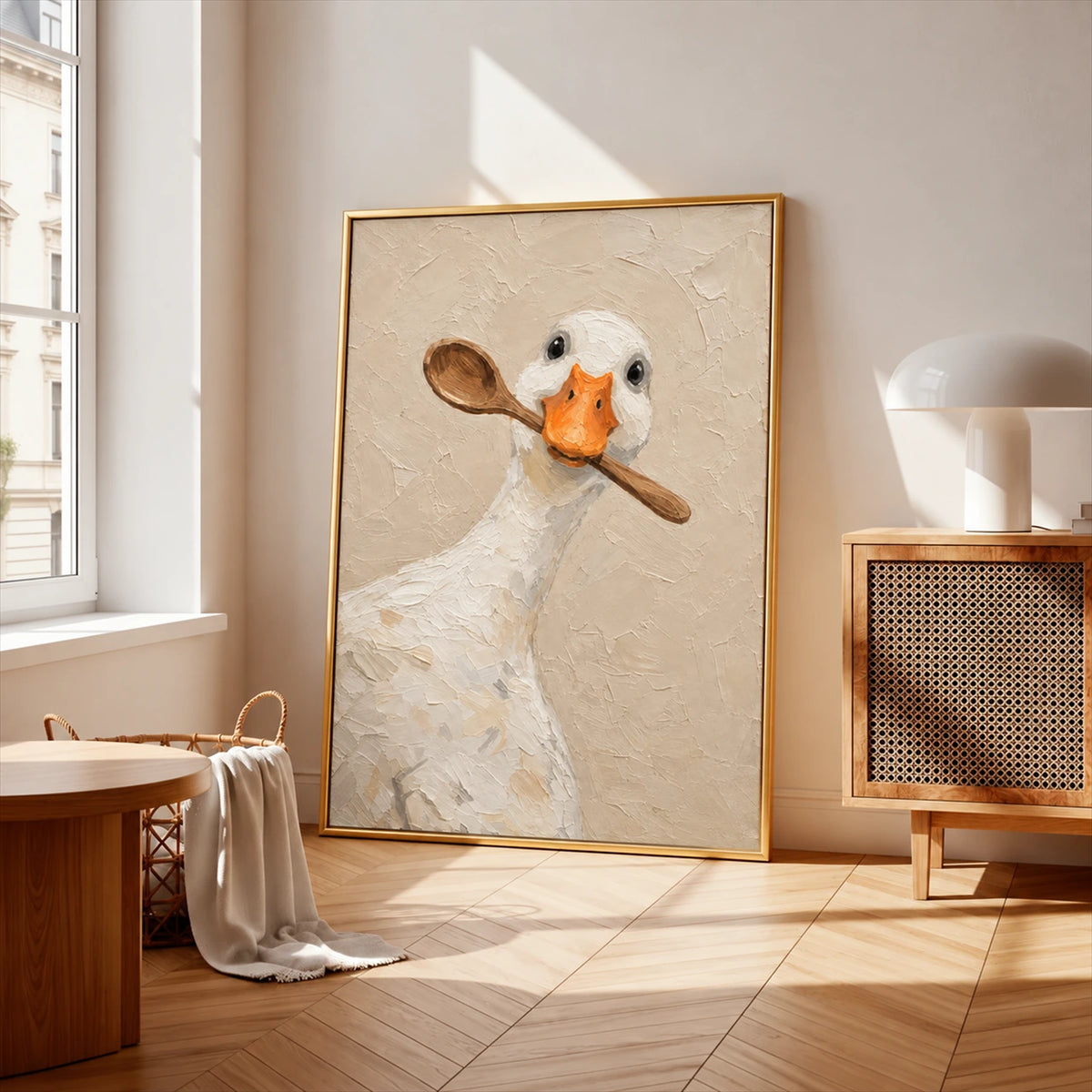 Gold-framed spoon duck painting leaning near a bright window beside a wood cabinet.