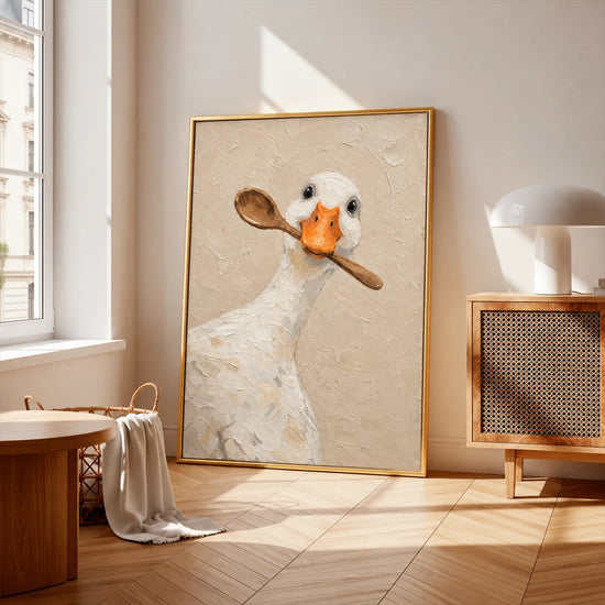 Gold-framed spoon duck painting leaning near a bright window beside a wood cabinet.