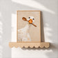 Spoon duck painting in a light wood frame resting on a scalloped wood shelf.