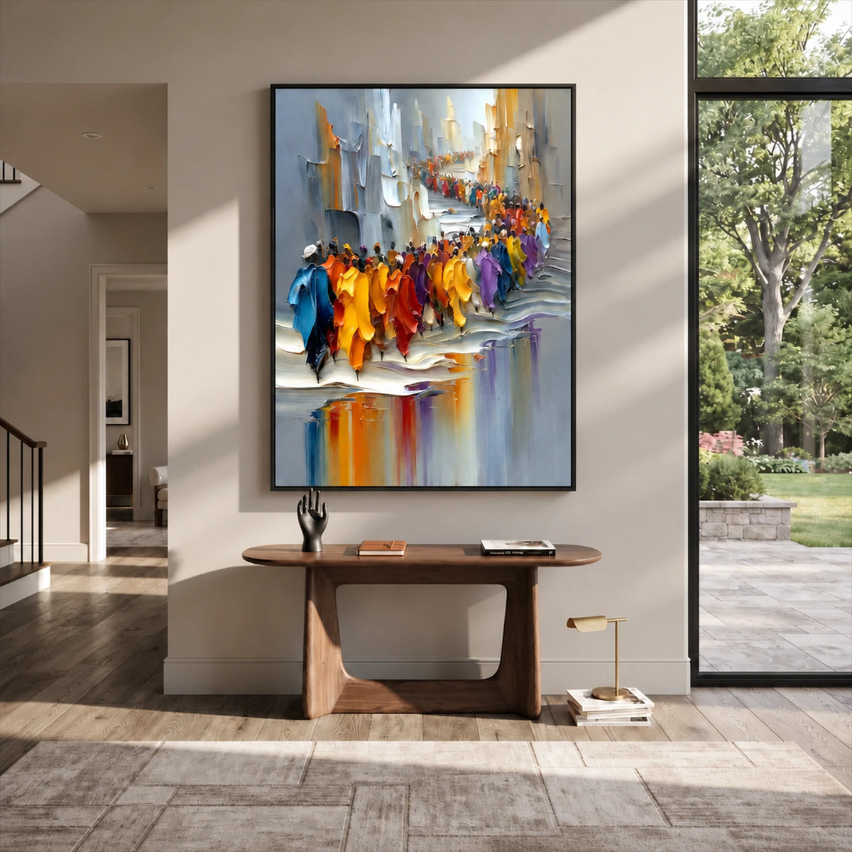 Colorful city procession painting in a dark frame above a sculptural wood console beside tall windows.