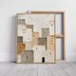 Neutral village painting in a light wood frame leaning in front of a reverse-facing canvas.