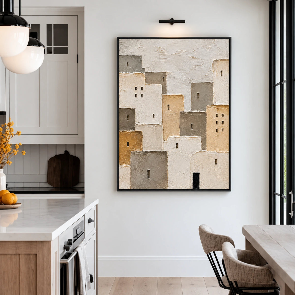 Neutral village painting in a black frame beside a kitchen counter and dining table.