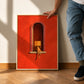Scarlet Reader painting in a thin light frame leaning against a wall beside a standing person.