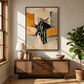 Ochre Reader painting above a wood sideboard with a lamp and books beside a leafy plant.