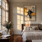 Ochre Reader painting above a bed with neutral linens in a bedroom lit by warm window light.