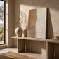 Unframed Sandstone Lines canvas leaning on a console beside a ceramic vase with bare branches.