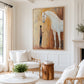 Gentle Bond painting in a bright living room with white seating, woven accents and a wood side table.