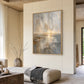 Gilded Horizon painting above a pale ottoman in a warm neutral living room.