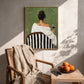 Evening Sip painting above a woven armchair beside a wood table with fruit and a book.