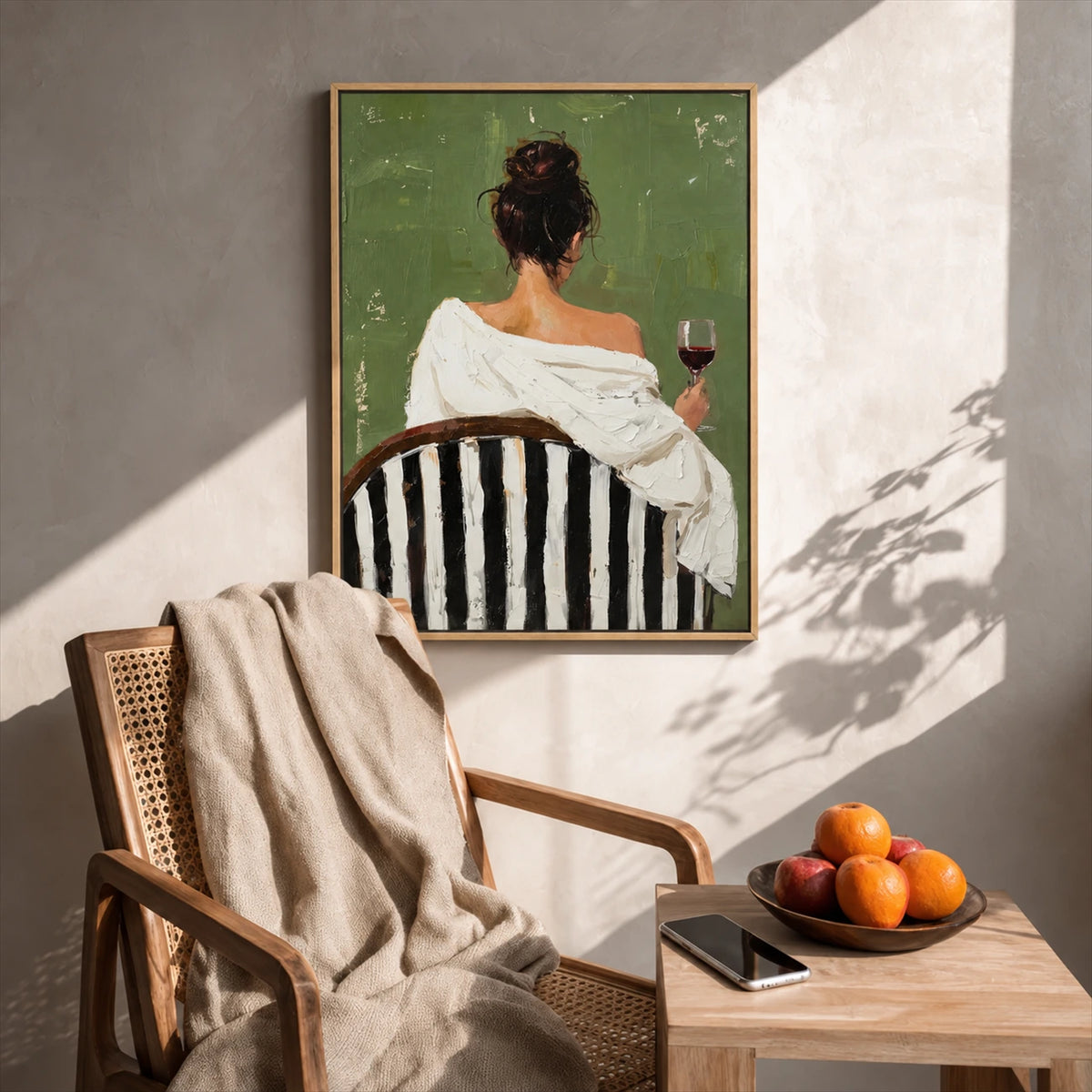 Evening Sip painting above a woven armchair beside a wood table with fruit and a book.