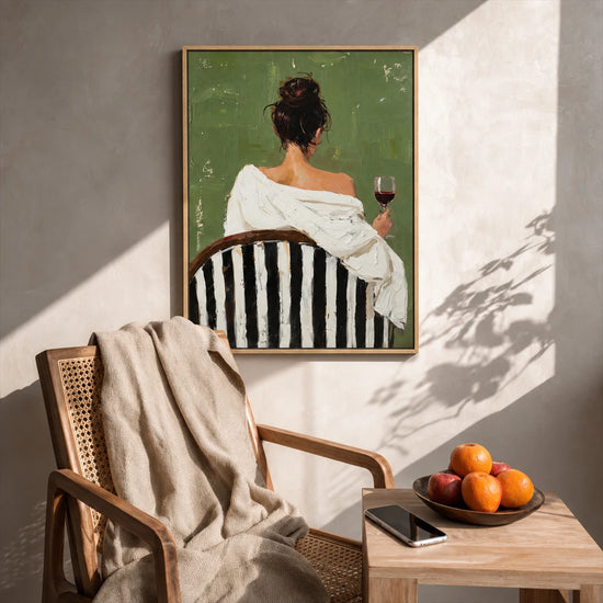 Evening Sip painting above a woven armchair beside a wood table with fruit and a book.