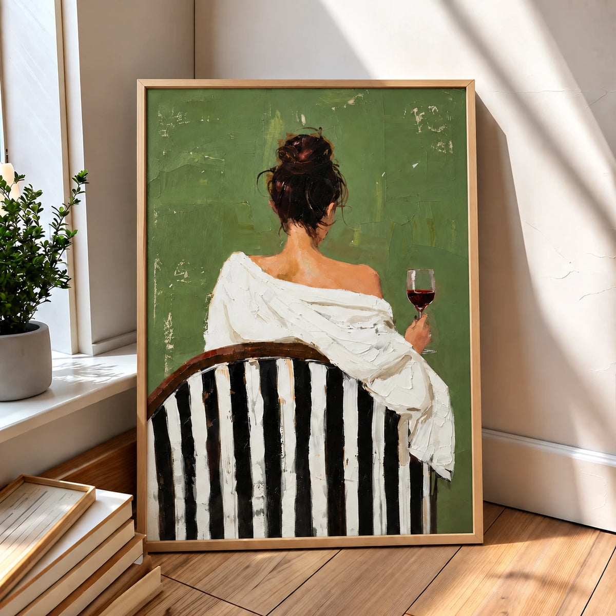 Evening Sip painting in a wood-colored frame leaning beside a sunlit window and a stack of books.