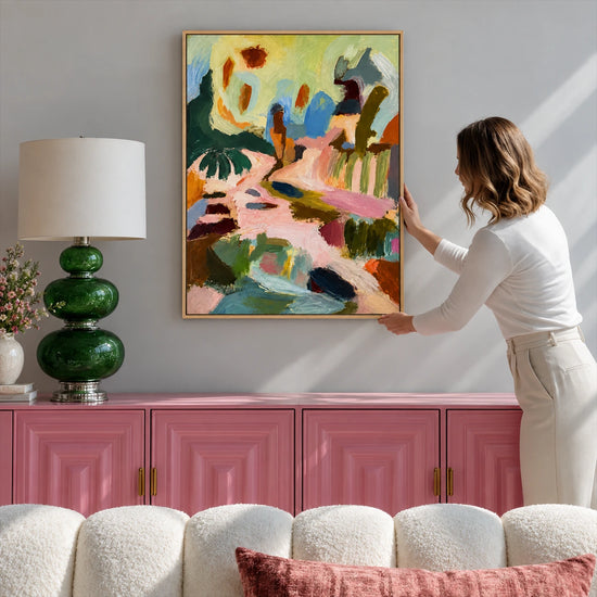 A person adjusting Pastel Reverie above pink wall paneling beside a green glass lamp.