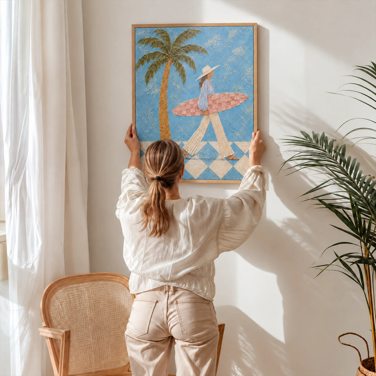 A person positioning Blue Palm Surfer on a light wall beside a woven chair and leafy plant.