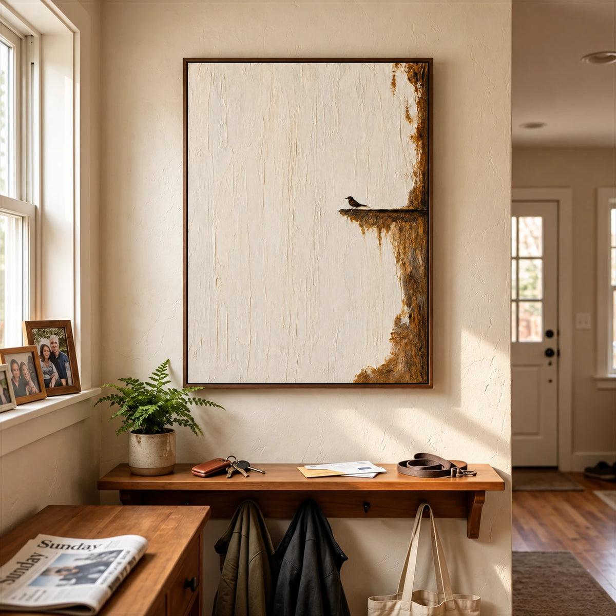 Quiet Perch painting above a wooden entry shelf with bags hanging beneath, beside a sunny window.