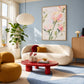 Blush Petals painting above a curved cream sofa in a blue room with a red coffee table and mustard chair.