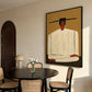 Ochre Stillness painting beside a round black dining table and woven chairs near an arched door.
