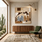 Coffee Companions painting above a wooden sideboard beside a green chair and a cactus-filled window.