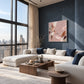 Blush Reverie artwork displayed above a white sofa beside tall city windows.