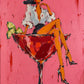 Cocktail Muse full artwork. A long-legged figure in a black hat perches on an oversized red cocktail glass against a vivid pink ground.