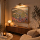 Pastel Highlands artwork displayed above a wooden sideboard beneath a picture light.