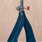 Indigo Stride full artwork. An elongated figure strides across a blush ground in sweeping indigo trousers and a black-and-white striped blouse.