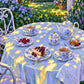 Garden Porcelain full artwork. Blue-and-white teacups, pastries, and a teapot rest on a softly draped garden table beneath flickering sunlight.