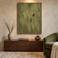 Olive Hover artwork displayed above a low wooden cabinet beside a green lounge chair.