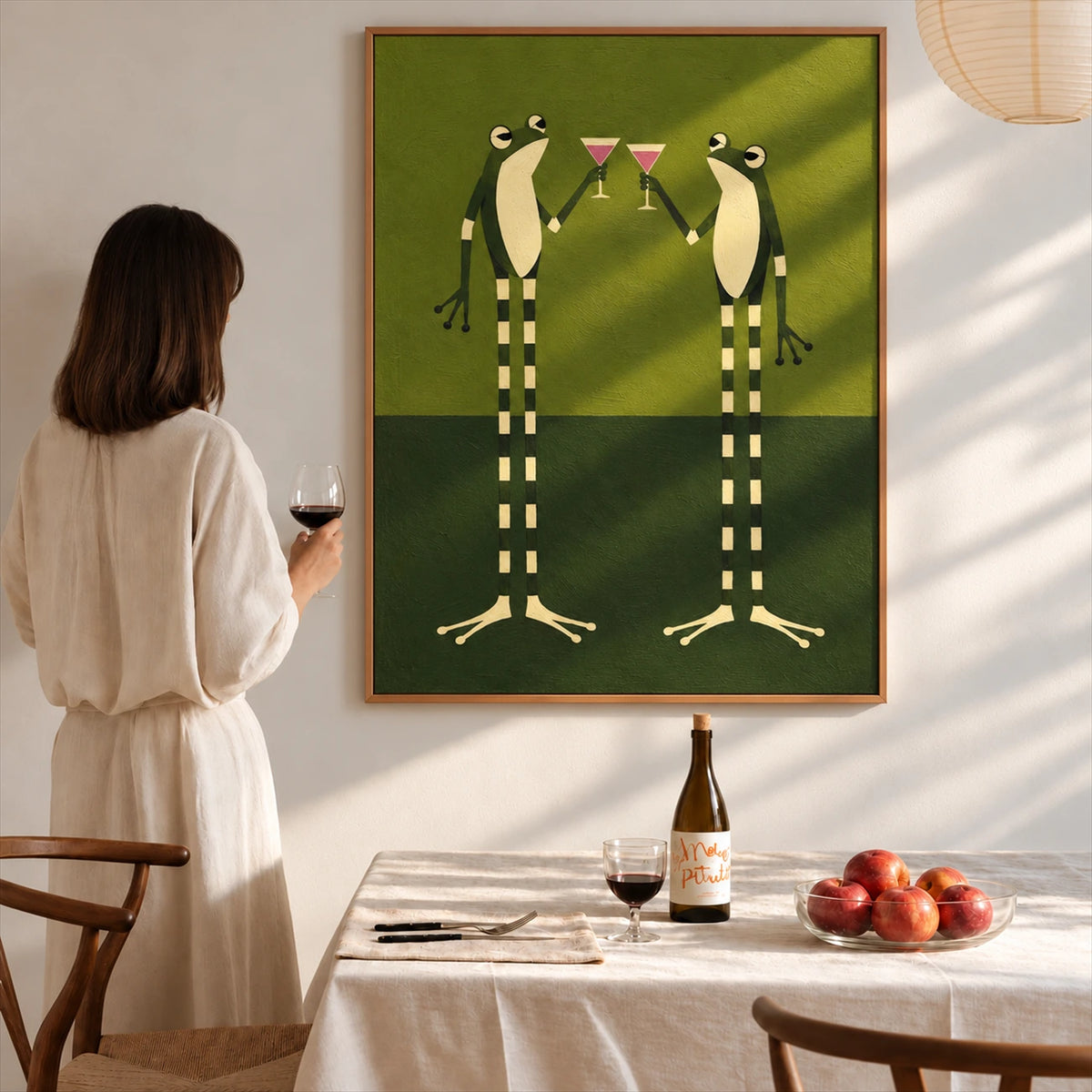 Frog Toast artwork displayed above a dining table beside a woman holding a wine glass.