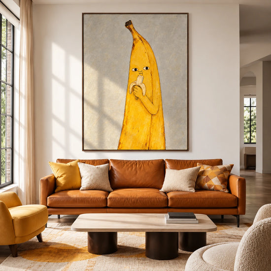 Banana Break artwork displayed above a caramel leather sofa in a bright living room.