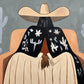 Cactus Siesta full artwork. A seated figure rests beneath a broad cream hat, wrapped in a dark shawl decorated with pale cactus and floral motifs.