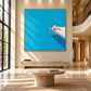 Turquoise Leisure artwork displayed above a stone console in a tall sunlit entryway.