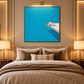 Turquoise Leisure artwork displayed above a bed beneath a picture light.