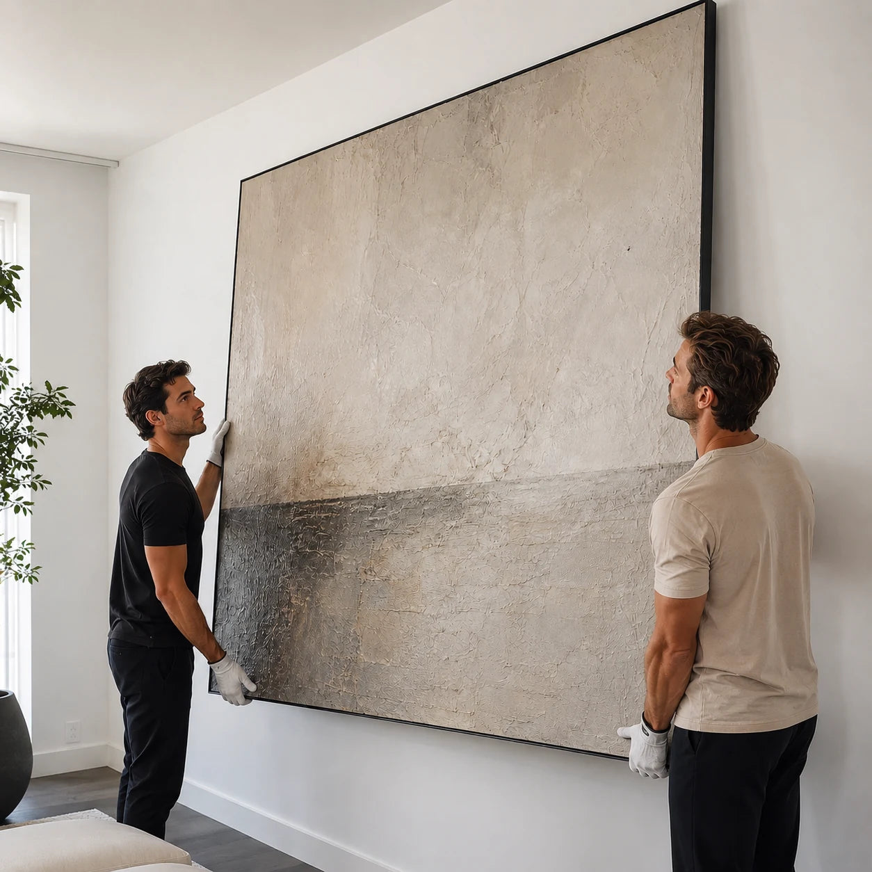 Two people positioning a large framed painting against a wall